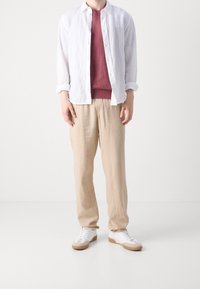 Avslappnad outfit med en vit linne skjorta, vinröd tröja, beiga linnebyxor och vita sneakers med gummisula.