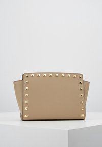 Beżowa torebka o zorganizowanym prostokątnym kształcie, zdobiona złotymi ćwiekami z przodu. Wykonana z teksturowanego materiału.