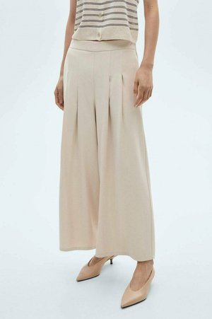 Beige weite Hose mit Falten, aus leichtem Stoff. Glatte Textur, hohe Taille, kombiniert mit hellen, spitzen Absätzen.