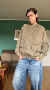 Veste zippée beige clair avec de grandes poches avant, capuche à cordon et poignets côte à côte. Associée à un jean en denim bleu délavé, ample.
