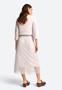 Lichtroze cropped trui met textuur breiwerk, gecombineerd met een geplooide, semi-transparante lichtbeige rok en chunky bruine haksandalen.