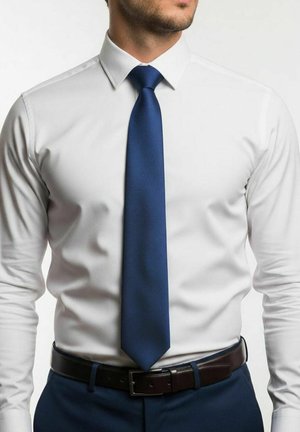 Witte overhemd met een puntige kraag, gecombineerd met een getextureerde donkerblauwe stropdas. Zwarte riem met een glanzende gesp, marineblauwe broek.