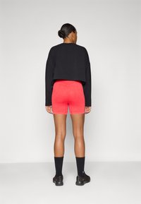 Black cropped sweatshirt, red fitted shorts, and black ankle socks with a logo. Smooth texture, casual design, and shorts have a seamless finish.