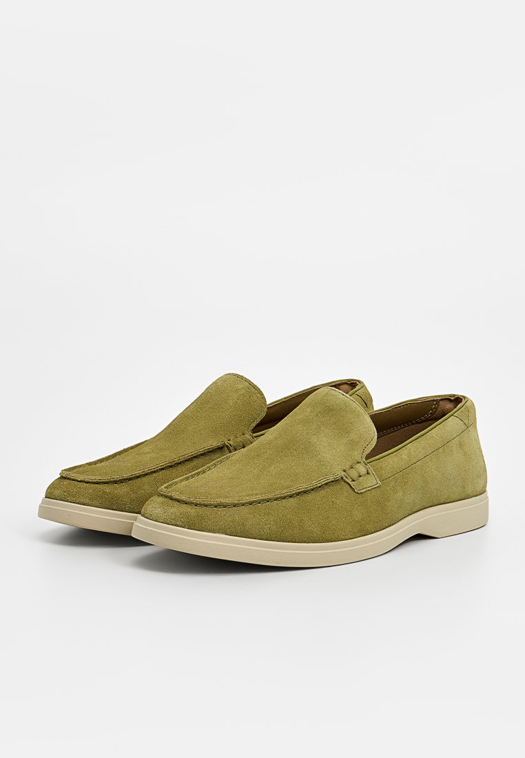 Bottines en daim vert olive à enfiler avec un bout arrondi, des coutures décoratives et une semelle en caoutchouc beige clair. Texture lisse, design décontracté.