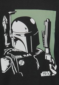 Schwarzes T-Shirt mit einer weißen Grafik einer helmetierten Figur, die eine Waffe hält, vor einem grünen quadratischen Hintergrund. "Star Wars"-Logo am unteren Rand.