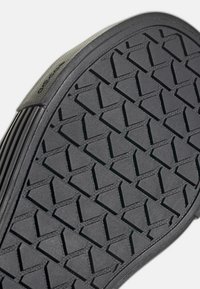 Suela de zapato de goma negra con patrón de tacos triangulares y costado texturizado visible sobre un fondo blanco.