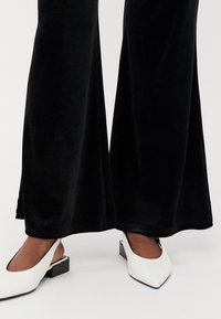 Zwarte fluwelen wijdpijpsbroeken met een gladde textuur. Gecombineerd met witte rechte slingback schoenen met blokhakken.