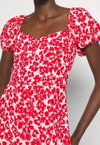 Rotes Blumenkleid mit kurzen Puffärmeln und quadratischem Ausschnitt. Verfügt über weiße Blumenmuster und geraffte Details an der Brust.