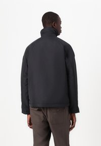 Black, insulated jacket with a high collar and structured design. Smooth texture, subtly visible stitching, and a minimalistic style.