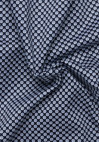 Marineblauwe stof met een klein wit bloemig geometrisch patroon, getoond met zachte plooien en een zachte textuur.