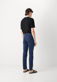 Pantaloni marini cu o croială mulată și buzunare laterale, asortați cu un tricou negru cu mânecă scurtă și sandale negre. Caracteristici cu detalii minime.