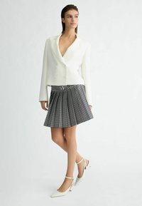 Witte dubbelgeknoopte blazer over een zwart-wit geruite geplooide rok, gecombineerd met witte puntige slingback hakken.