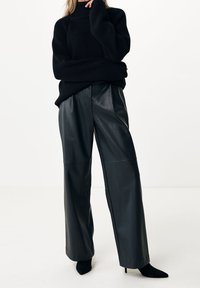 Pull en maille côtelée noire avec un col montant, associé à un pantalon large en similicuir noir et des escarpins noirs à bout pointu.