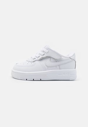 Biały niski sneaker z sznurowadłami i paskiem na rzep, z logo Nike po boku oraz teksturowaną podeszwą, pokazany z profilu na białym tle.