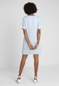 Ljusblå linnklänning med korta ärmar och rak skärning, med sydda detaljer längs fållen. Bärs med vita klackskor med blockklack.