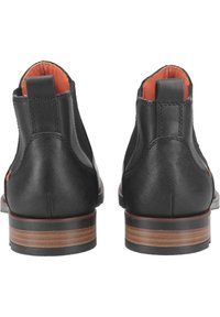 Botas de tobillo de cuero negro con un acabado texturizado, forro naranja, tiradores y tacones de madera marrón. Diseñadas para un uso fácil y comodidad.