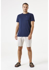 Marineblauw katoenen t-shirt met een borstzak, gecombineerd met licht gestreepte shorts. Zwarte sandalen maken de casual outfit compleet.