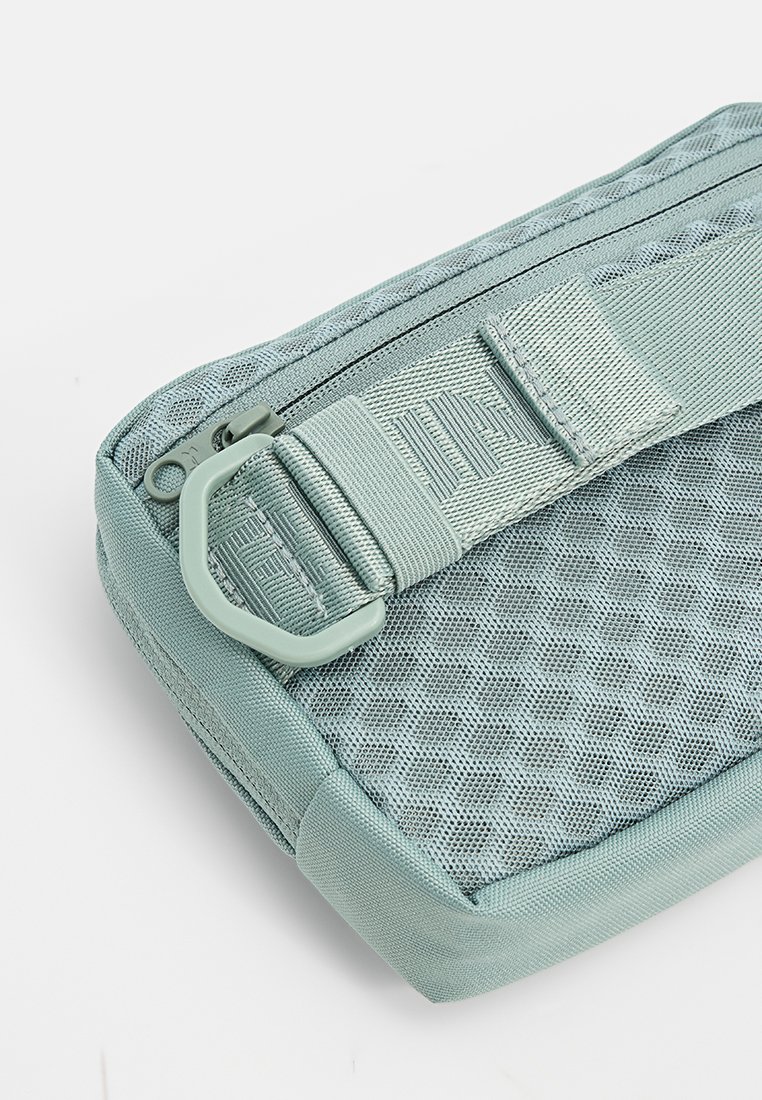 Bolsa de malla y tela azul claro con cremallera, correa ajustable y detalle de hebilla de plástico sobre fondo blanco.