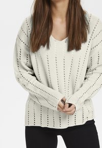 Light grey knitted sweater with a V-neck, featuring openwork stripes and long sleeves. Soft texture, ribbed cuffs, and a relaxed fit.