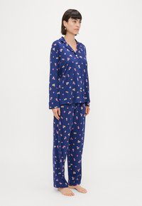 Conjunto de pijama floral azul-marinho com mangas compridas, camisa de botões e calças largas, com uma textura suave e macia e um padrão colorido de flores.