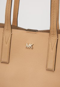 Sac à main en cuir grainé marron clair avec des anses cousues et un petit logo MK doré centré près du bord supérieur.