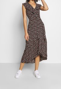 Vestido negro con estampado floral, con mangas acampanadas y volantes, escote en V y dobladillo asimétrico, que presenta pequeños patrones rojos y blancos. Combinado con zapatillas blancas.