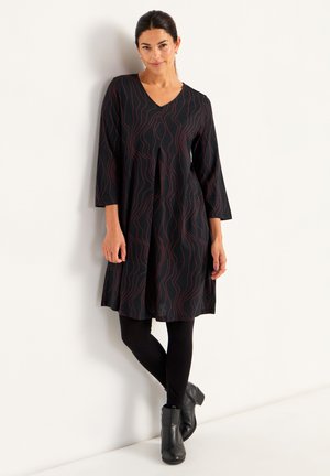 Black knee-length dress with red wave pattern, V-neckline, 3/4 sleeves, and flared design, paired with black leggings and ankle boots.
