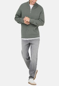 Minzgrüner Reißverschluss-Pullover mit gerippter Textur, kombiniert mit hellgrauen Jeans und weißen Sneakers mit beigen Akzenten.