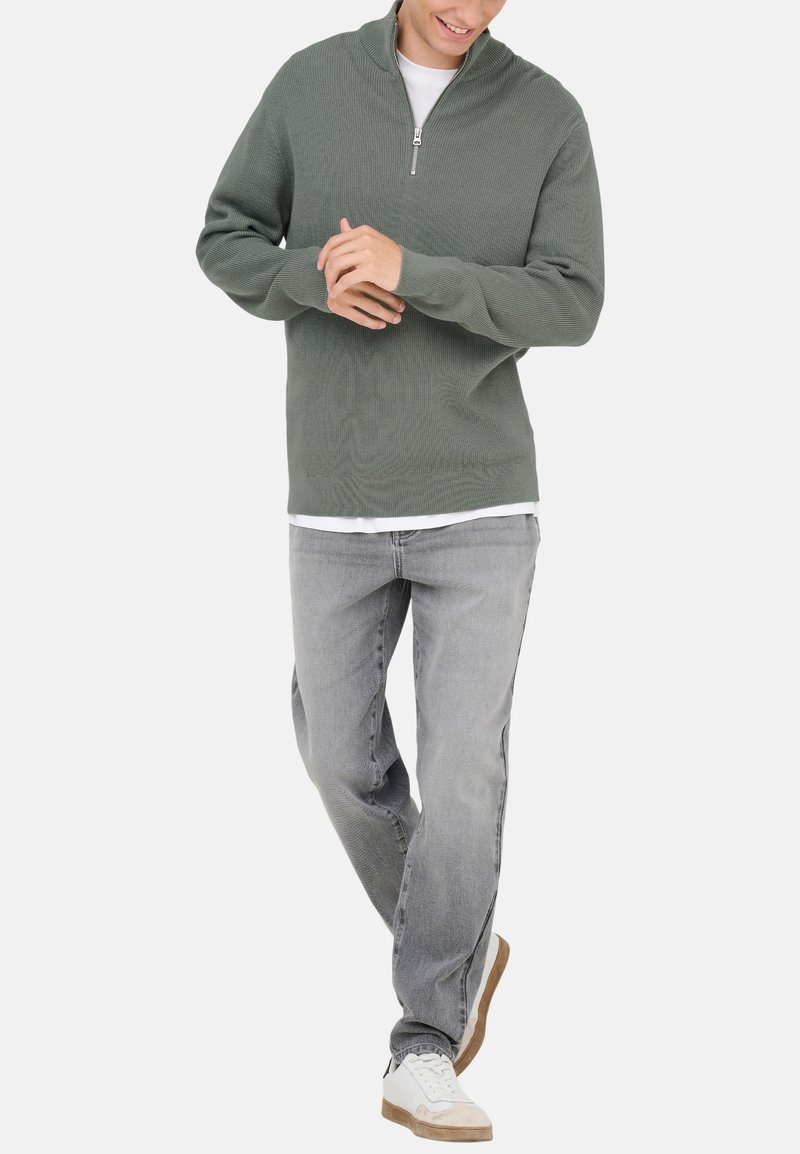 Minzgrüner Reißverschluss-Pullover mit gerippter Textur, kombiniert mit hellgrauen Jeans und weißen Sneakers mit beigen Akzenten.