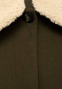 Chaqueta de mezcla de lana con un cuello de borreguito beige, que presenta un solo botón negro y un cuerpo texturizado de color verde oscuro.