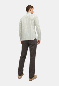 Chemise à manches longues vert clair à motifs avec une coupe décontractée, associée à un pantalon gris foncé et des chaussures à enfiler beiges. Détails en tissu texturé visibles.