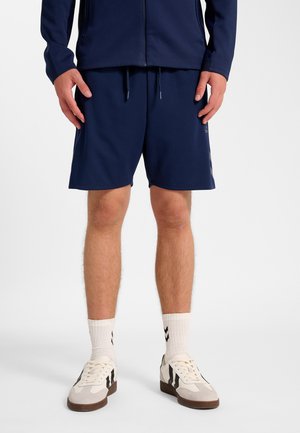 Marineblå atletikshorts med elastisk linning og snøre. Kombineret med lyse sneakers og mønstrede sokker, på en neutral baggrund.