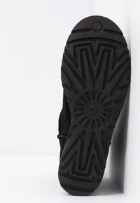 Semelle d'une botte noire avec des motifs de bande de roulement en zigzag profond et radiaux, conçue pour la traction et la durabilité.