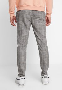 Grå rutiga byxor med slim fit, med tunna linjer i röd och vit, kombinerat med vita sneakers och en persikofärgad sweatshirt.