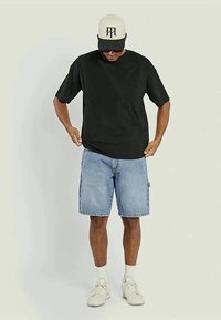 Black short-sleeve t-shirt paired with light blue denim shorts, white athletic shoes, and a beige cap with a black logo.