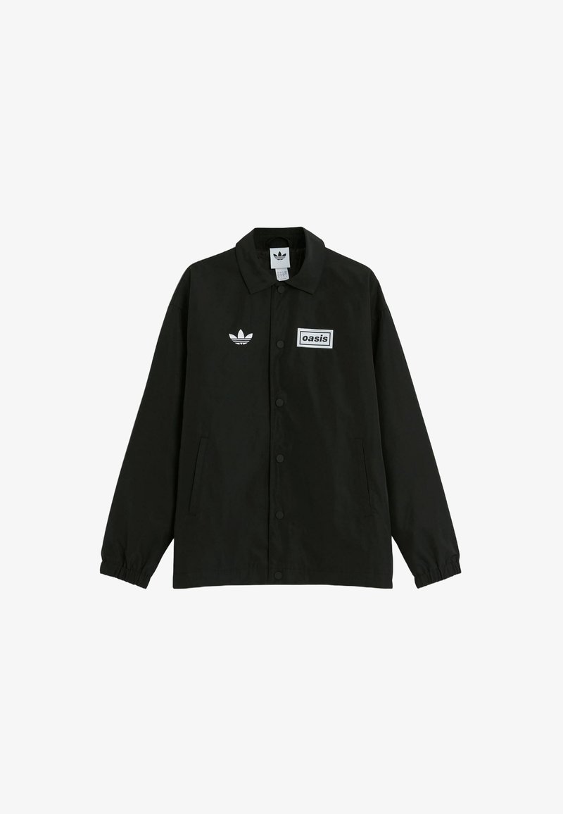 Black button-up jacket made of smooth fabric. Features a white rectangular patch with "oasis" text and Adidas logo on the chest.