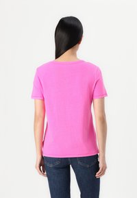 Tricou scurt cu mâneci, de culoare fucsia, cu decolteu rotund, din material bumbac și croială lejeră, asociat cu jeansi de culoare albastru închis.