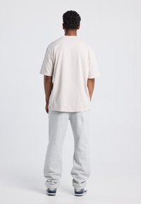 Light gray oversized t-shirt with short sleeves, made from soft cotton, paired with loose-fitting gray sweatpants and dark athletic shoes.