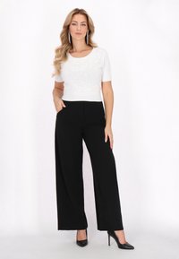 Weißes Kurzarmtop mit Pailletten, kombiniert mit schwarzen weit geschnittenen Hosen. Glatte Texturen und elegante High-Heels runden das Outfit ab.