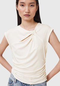 Crème-kleurige top met korte mouwen en een geknoopte detail bij de halslijn, met een geplooide textuur, gecombineerd met lichtblauwe denim.