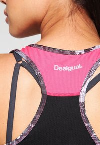 Zwarte en roze sporttop met verstelbare bandjes, gestructureerde stof en een bedrukte halslijn. Logo op de achterkant.