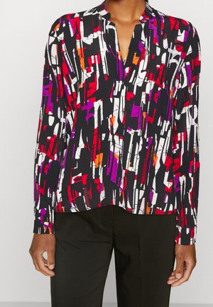 Blusa de manga larga con patrón geométrico abstracto en negro, blanco, rojo, púrpura y naranja, combinada con pantalones negros lisos.