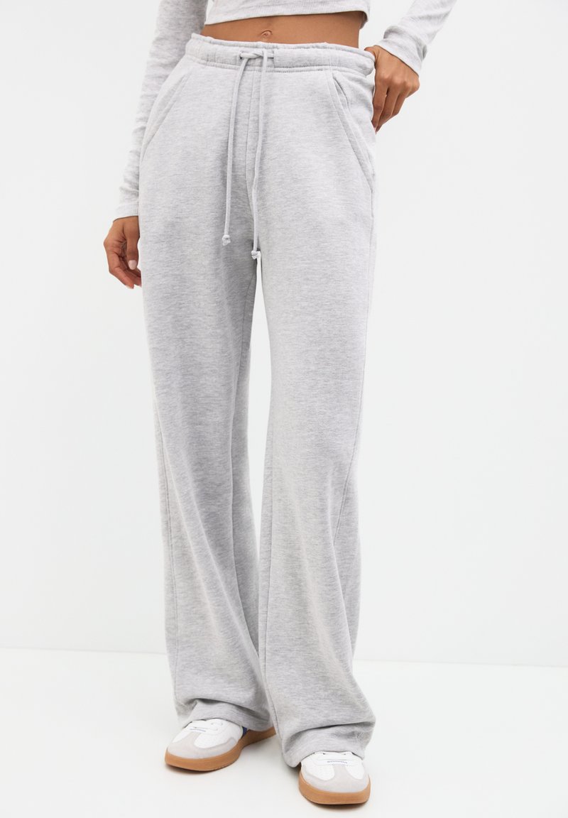 Hellgraue Sweatpants aus weichem Material, im weit geschnittenen Design, mit Kordelzugbund und Taschen seitlich, kombiniert mit weißen und hellbraunen Sneakern.