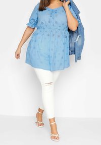 Niebieska bluzka z krótkim rękawem z kwiatowymi wycięciami, w połączeniu z białymi, podartymi obcisłymi dżinsami oraz białymi sandałami na ramiączkach, dopełniona jeansową kurtką.