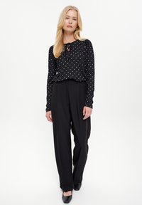 Czarny top z długim rękawem w białe kropki z detalem w postaci wiązania przy dekolcie, zestawiony z czarnymi szerokimi spodniami i czarnymi balerinami.