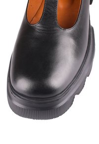 Chaussure en cuir noire avec bout arrondi, semelle épaisse à rainures, et deux larges découpes sur le dessus laissant apparaître une doublure intérieure marron.