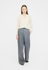 Light beige long-sleeve blouse with a V-neck, paired with grey wide-leg trousers featuring a textured fabric and subtle pleats.
