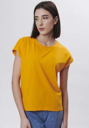 Gul bomulds T-shirt med korte, rullede ærmer og rund hals. Glat tekstur, afslappet pasform, kombineret med blå denim jeans.
