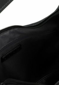 Intérieur d'un sac en cuir noir, avec une doublure lisse, une poche zippée et des accents cousus. Sa forme est rectangulaire avec un design minimaliste.