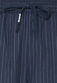 Granatowe szorty ze sznurkiem do regulacji, wykonane z teksturowanej tkaniny, z cienkimi białymi paskami i plecionym sznurkiem do regulacji obwodu w talii.